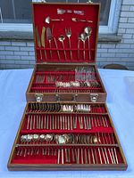 Open teak wood box with three red-felt lined trays filled with brass flatware