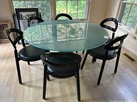 Six chairs arranged around a glass-top table by a window