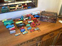 Wide view of the collection showing multiple Lesney diecast cars arranged on wooden cabinet with wooden chest on the right