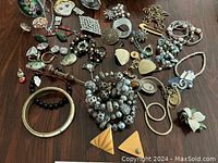 Overall view of assorted jewelry pieces laid out on table including necklaces, bracelets, earrings, brooches, rings.