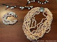 All items displayed on a wooden surface: multi-strand pearl necklace, multi-strand pearl bracelet and two brown cord pearl bracelets