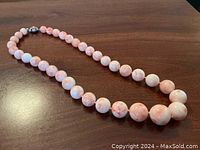 Full view of graduated pink and white coral bead necklace laid flat.