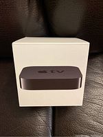 Front view of the white retail box showing an image of the Apple TV unit with Apple TV text on top and bottom of box.
