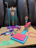 Full view of Barbie gymnastics dolls with uneven bars, balance beam, trophy, and accessories on dark backdrop