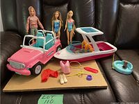 Photo of entire lot including Barbie jeep, boat, three dolls, and various accessories on cardboard