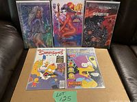 Photo showing five comic books covering Coven, Simpsons, and Kiss Psycho Circus placed on a cardboard box on a black surface