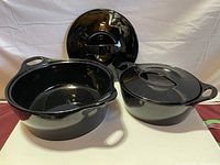 Two black Corningware Creations stoneware dishes with lids, showing one lid leaning against the other dish.