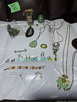 Full lot overview showing jade egg, assorted necklaces, earrings, bracelets, and pins on white background.