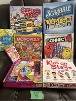 Multiple boxed kids games arranged on a chair including Guess Who?, Scrabble Junior, Monopoly Junior, Connect 4, Chutes and Ladders, and Kids on Stage.