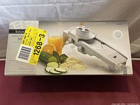 Box of Kuraidori Multi Purpose V-blade Mandolin showing product image and sliced vegetables.