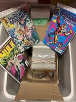 Top-down view of bin containing bagged and boarded Marvel comics in cardboard box showing Spectacular Spider-Man, The Incredible Hulk, purple backing board.