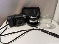 Nikon L35AF camera with additional lens, lens cap, clear plastic lens hood, and black carrying case on white surface.