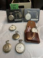 Two Victoraville pocket watches in plastic boxes at top, five loose pocket watches at bottom, leather pouch visible