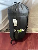Sleeping bag stored in black nylon compression sack with 'Protex' logo visible and attached tag.