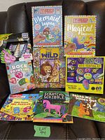 Photo shows the full collection of the lot including rock painting kits, activity books, and unicorn horn chalk set all arranged on a chair.