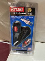 Front view of Ryobi 15-Blade Nack Cutter in unopened plastic packaging showing the tool and red rotary blade cartridge, with clear Ryobi branding and usage claims on the label.