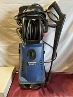 Front view of the blue Simoniz pressure washer showing the 1700 PSI label. Power cord wrapped on top and spray gun attached.