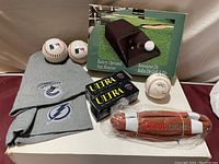 Overview photo of all items in lot including electric putt returner in original box, baseballs, football, and two toques