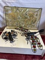 Photo showing stained glass framed wall art and two metal insect garden decor pieces on a white surface