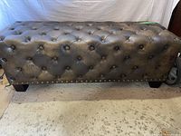 Full side view of the brown tufted faux leather ottoman showing overall shape, size, and condition.