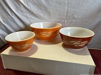 Three vintage Pyrex Autumn Harvest nesting bowls side by side on box showing exterior wheat design and color variation