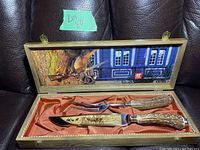 Full view of the set inside the original wooden box showing the knife, fork, orange satin interior lining, and the lid with decorative print and logo