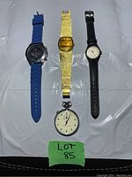 Full view of three wrist watches and one stopwatch on white background with lot number