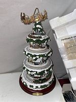 Full view of the Wonderland Express Christmas tree showing all three tiers, snow-covered foliage, miniature village scenes, and the moving train around the base. Certificate of authenticity and styrofoam packaging visible in background.