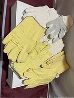 Yellow leather gloves, white fabric gloves, and white gloves with gray leather palms visible in the lot