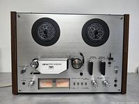 Front view of AKAI GX-4000D deck on table showing reels, control knobs, VU meters and wood side panels