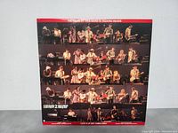 Front of album cover showing multiple rows of band members performing live on stage with black background and red border.