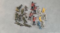 Image showing all 19 toy soldiers laid out on surface including metal and plastic figures with British guards in red jackets and various standard army poses.