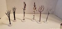 Front view of six 1990s holiday village display trees in brown and white, standing side by side on a flat surface.