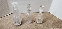 Photo showing three crystal decanters side by side on carpet, each with unique stopper and decorative patterns.