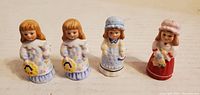 Front view of the four porcelain figurines depicting girls in dresses, showing details and colors.