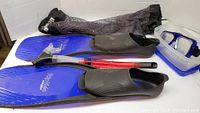 Photo of snorkeling gear showing blue Deep Blue Rip Tide flippers, black and red snorkel, blue mask, and black mesh bag.
