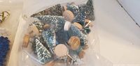 A clear plastic bag containing several green bottle brush Christmas trees with white snow flocking and wooden bases in varying sizes from 4 to 7 inches.