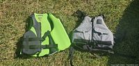 Two adult XXL flotation devices, lime green-grey and grey, lying on grass.