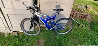 Side view showing blue and silver dual suspension mountain bike leaning against a shed with grass ground.