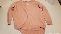 Front view of peach-colored TJ Maxx long sleeve sweater laid flat with tag attached on neckline area
