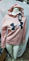 Photo of a women's peach Under Armour hoodie on a mannequin showing front view with logo and attached tag.
