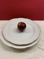 Two white porcelain platters stacked, apple placed on top for size scale against red background.