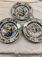 Group view of three porcelain plates laid on cloth, showing overall decoration and condition.