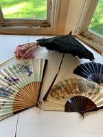 View of antique fans and parasols on a windowsill, showing general condition and designs.