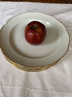 Stack of five white porcelain dinner plates with scalloped edges and gold trim, apple placed on top for scale