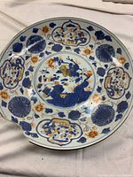 Top view of the large Asian charger plate showing full hand-painted floral and figural design with blue and orange colors and visible rim damage.