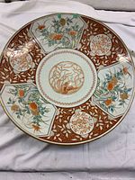 Front view of the large antique Asian decorative plate showing the intricate floral and fish designs in rust red, gold, and multi-color sections.