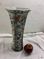 Tall hexagonal ceramic vase with colorful floral patterns and an apple next to it for scale.