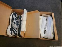 Both pairs of New Balance sneakers in their boxes, showing the left shoe of each pair, tissue paper inside, clean and unworn appearance.