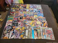 Overview of comic books spread on couch, showing a variety of colorful covers including X-Men, Superman, and Batman titles.
